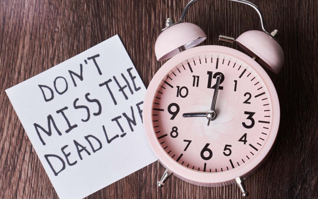 Old-fashioned alarm clock with a note next to it that reads Don't Miss The Deadline