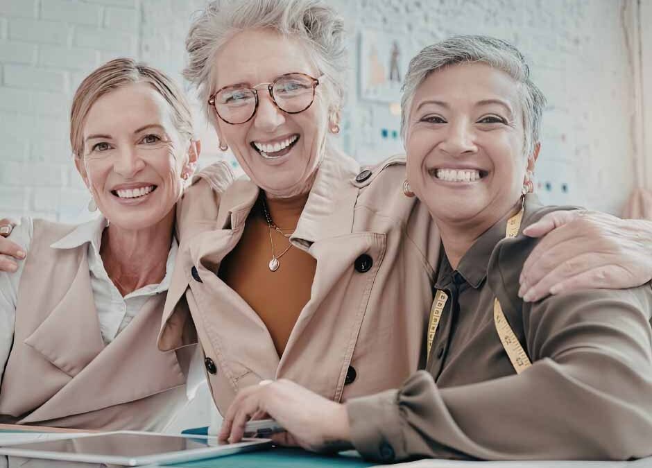 Three women smiling and sitting together at a table, enjoying each other's company in a cheerful atmosphere